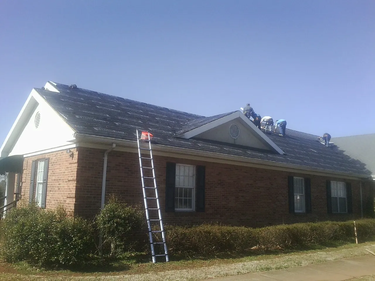 Crew tearing shingles off a brick ranch roof with a ladder set — Metal Roof Repair work by our crew in Riverton